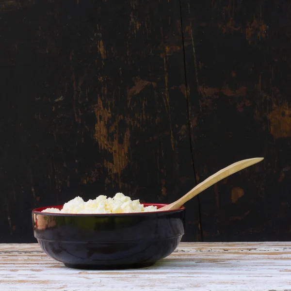 Black plate with yellow fresh cheese and juniper spoon on white wooden table. side view close-up. selective focus. square photo