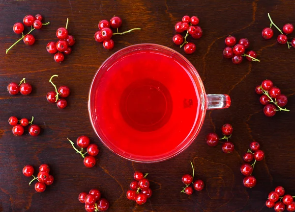 Freshly squeezed red juice, and bunches of red currants on a brown wooden table with old paint. closeup flat lay