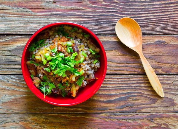 Wooden spoon and plate with buckwheat porridge with meat and herbs on an old wooden background close-up view from above. Rustic style. Russian cuisine