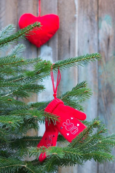 Mittens knitted from camel wool red color decorated with red rhinestones hearts bunnies on the branch of a Christmas tree on a background of old boards and Christmas toys in the shape of a heart