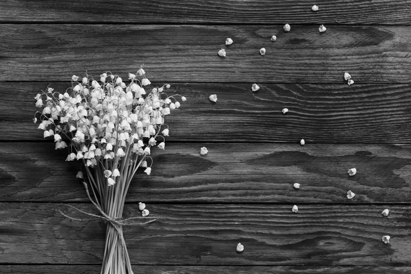 A bouquet of white flowers Lily of the valley and fallen buds on wooden boards in black and white