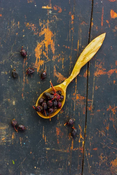 Dried rose hips in a wooden spoon on the old black background. Ingredient for cooking healthful beverage. The concept of rustic herbal therapy. Ingredient for cooking healthful beverage
