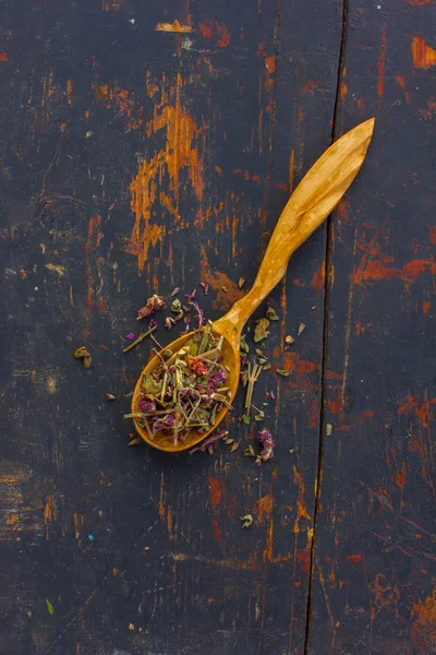 Dried herbs (Salvia officinalis) in a wooden spoon on the old cracked black background. Ingredient for cooking healthful beverage. The concept of rustic herbal therapy. Ingredient for cooking healthful beverage
