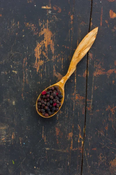 Dried hawthorn berries in a wooden spoon on the old cracked black table. Ingredient for cooking healthful beverage. The concept of rustic herbal therapy