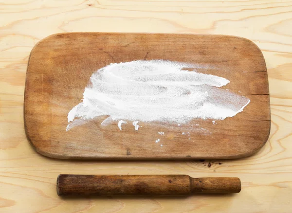 The old rolling pin and a wooden cutting Board with flour on wooden table