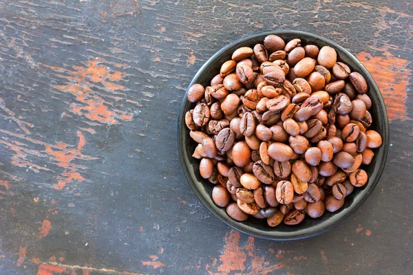 Roasted coffee beans in a round black saucer on old wooden background. Copy space. Free space for text, Close-up, top view