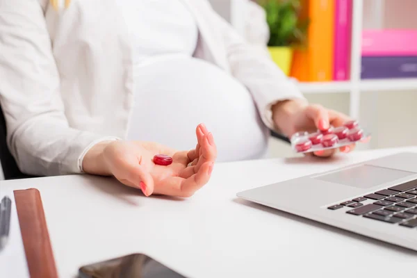 Pregnant woman in office taking medicine while working