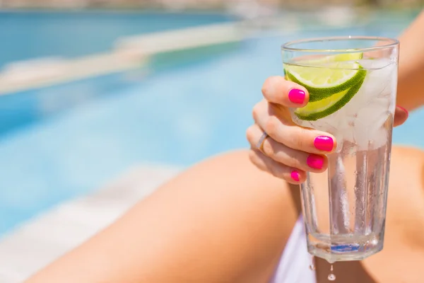 Woman holding refreshing cold drink while sunbathing by the pool