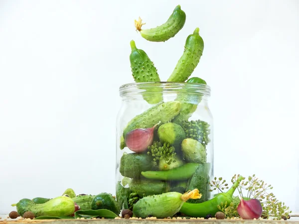 Cucumbers with herbs and spices for pickling in glass jar with flying ingredients on a white background.