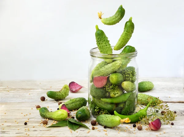 Cucumbers with herbs and spices for pickling in glass jar with flying ingredients on a white background.