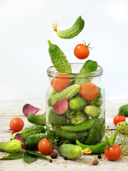 Cucumbers and cherry tomatoes with herbs and spices for pickling in glass jar with flying ingredients on a white background.
