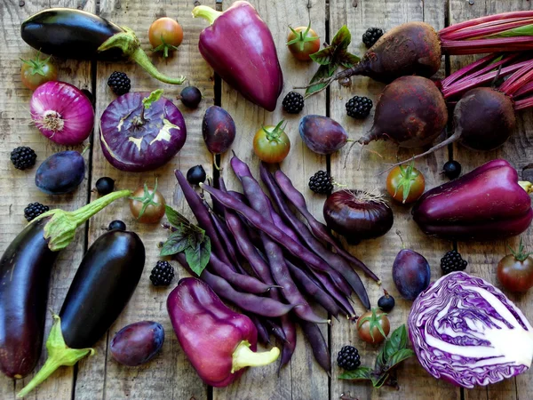 Purple vegetables and fruits on wooden background - eggplant, cauliflower, green beans, cherry tomatoes, plum, basil, onion, cabbage, sweet pepper