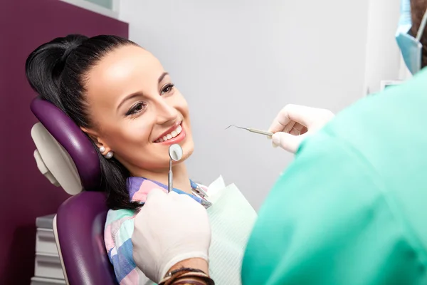 Woman sitting in dental chair while doctor examining her teeth.