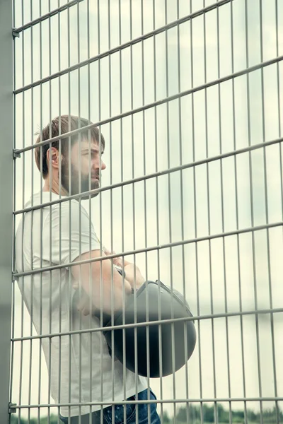 Biker men with beard in white shirt standing near fence