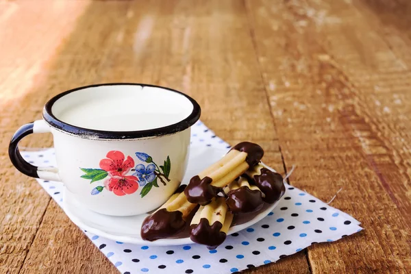 Homemade churros (finger biscuits) with mug of milk on wooden ta