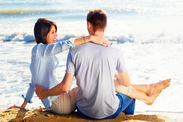 Couple Sitting on Sand at the Beach looking the sea