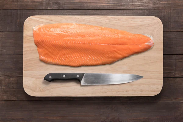 Fresh salmon and knife on cutting board on the wooden table. Top