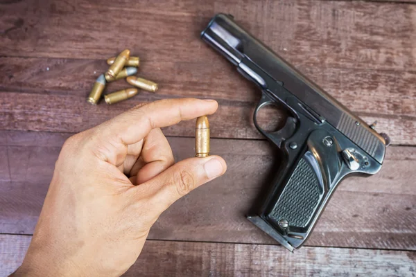 Hand with bullet and Semi-automatic 9mm gun on wooden background