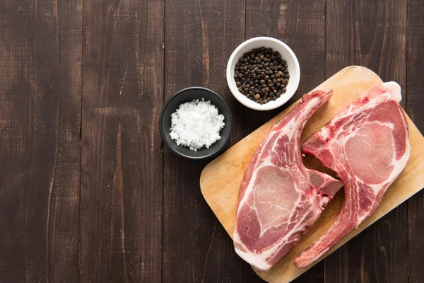 Fresh pork chops with pepper and salt on wooden background