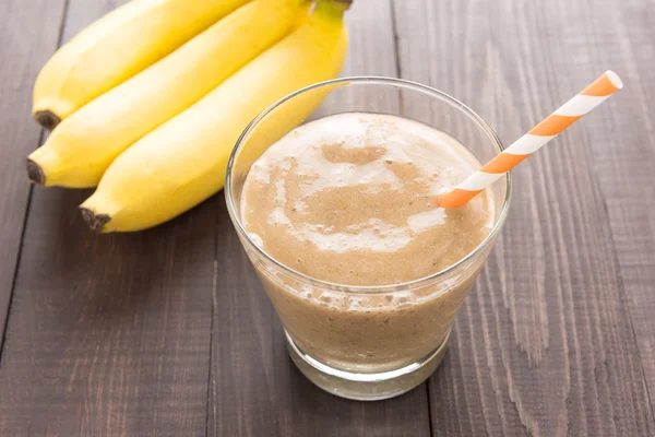 Banana smoothie and fresh banana on wooden background