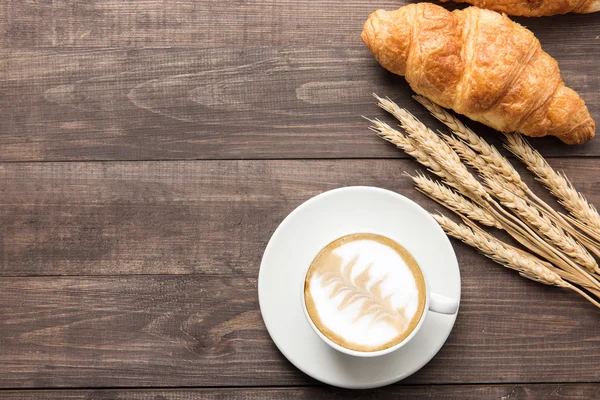 Coffee cup and fresh baked croissants on wooden background. Top