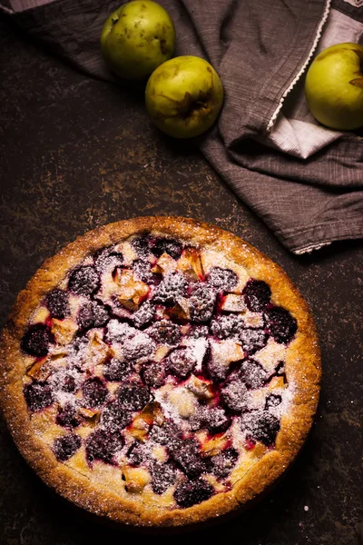 Homemade pie with apples and blackberry on dark stone background.