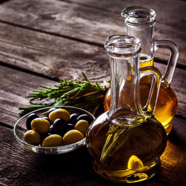 Two  bottles of olive oil, olive in a bowl and herbs on a wooden table.