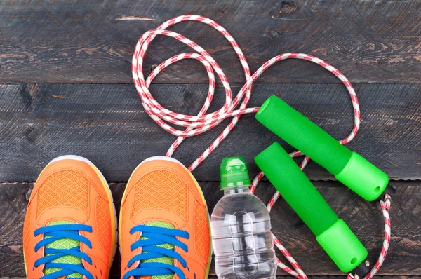 Sport shoes, skipping rope and bottle of water on the old wooden