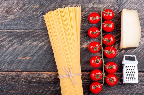 Spaghetti, tomatoes, cheese and grater on old rustic background.