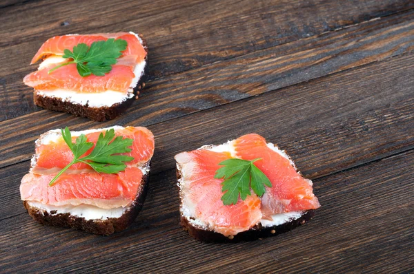 Sandwiches with salmon, cream cheese and parsley on a wooden table. Healthy food for breakfast or snack.