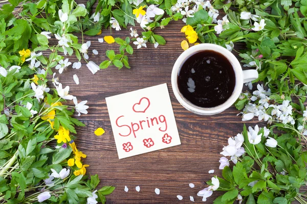 Cup of coffee on spring background. Coffee, flowers, note with word spring on a wooden surface