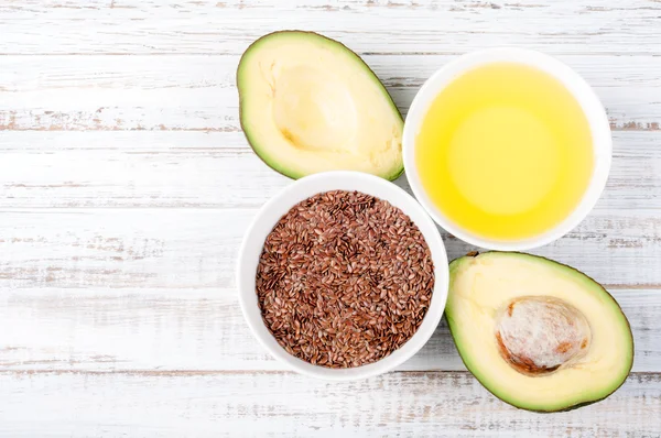 Foods with healthy fats. Sources of omega 3 - avocado, olive oil and flax seed on wooden background with copy space