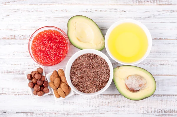 Foods with healthy fats. Sources of omega 3 - avocado, olive oil, red caviar, nuts and flax seed on wooden background. Healthy food concept