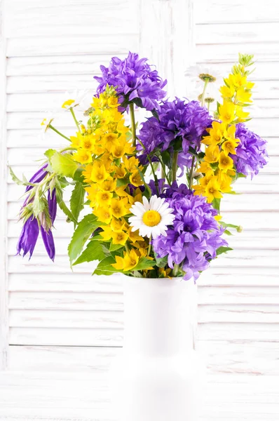 Bouquet of wild flowers  in a vase on white wooden background