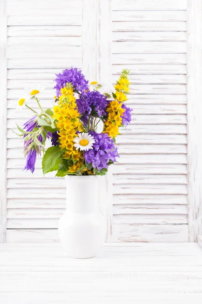 Bouquet of wild flowers  in a vase on white wooden background
