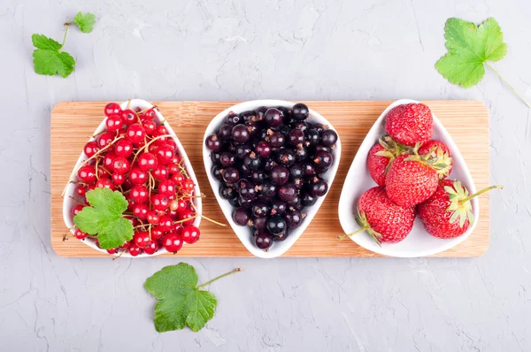 Berries mixed strawberries, currant and red currant in bowls on stone table. Summer berries background. Harvest concept