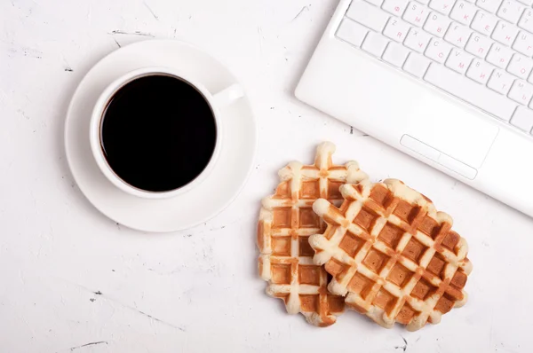 Coffee break concept. Workplace. Desk table with laptop, coffee cup and waffles on light background with copyspace