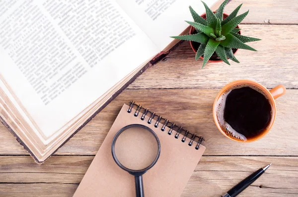 Coffee cup, open book, succulent aloe, pen, notebook and magnifier on rustic wooden background. Office desk table. Educations concept