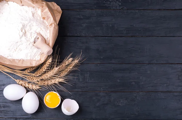 Baking background. Flour in paper bag, wheat and eggs on dark wooden table. Ingredients for cooking homemade baking