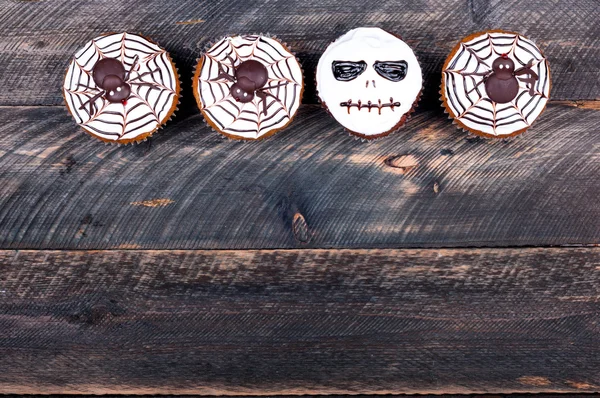 Halloween background. Funny pumpkin muffins with spiders and scull for halloween party on old rustic wooden table. Copy space