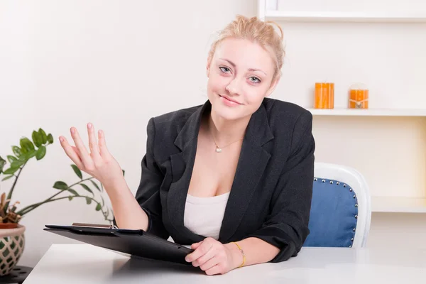 Pretty woman in a jacket gesturing at desk at work