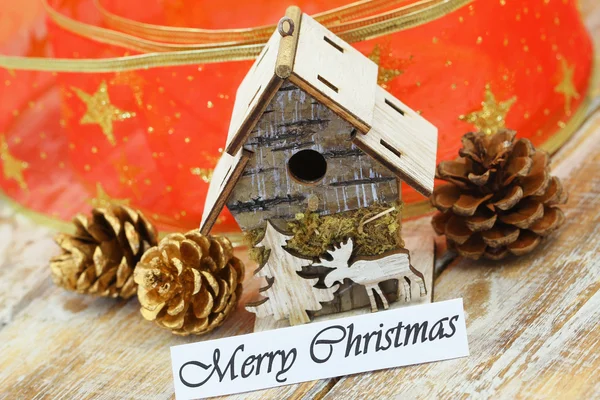 Merry Christmas card with miniature bird feeder, pine cones, and red ribbon