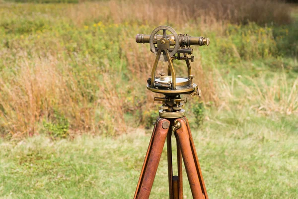 Close up of Vintage Surveyor\'s Level (Transit, Theodolite) with wooden Tripod in a field.