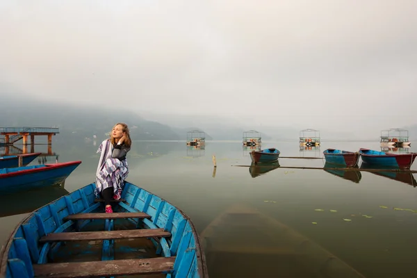 Girl sitting in old boat on mountain lake early morning