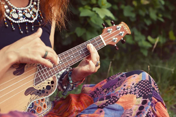 Beautiful young hipster or hippie woman in colorful clothes  playing ukulele