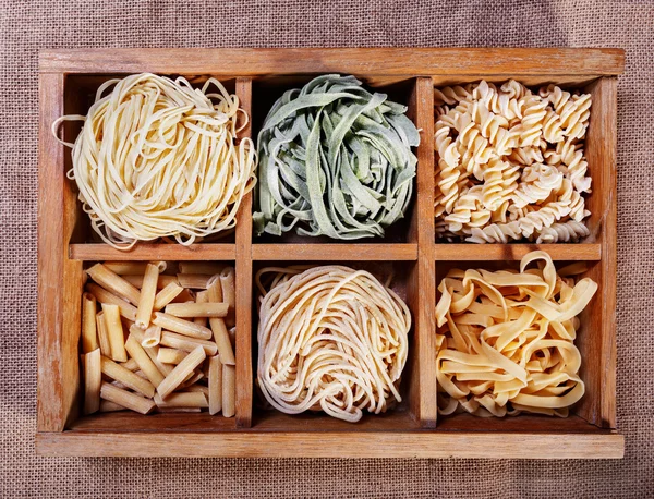 Assorted pasta in wooden box catalog on dark fabric background