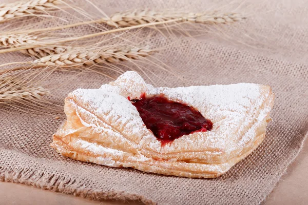 Fresh puff pastry with powdered sugar with jam on rustic background with spikelets. Pastries and bread in a bakery
