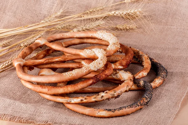 Fresh Pretzels with poppy seeds, cinnamon, sunflower seeds and sesame seeds on rustic background with spikelets. Pastries and bread in a bakery. Selective focus