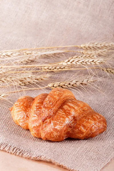 Tasty croissant with jam on rustic background with spikelets