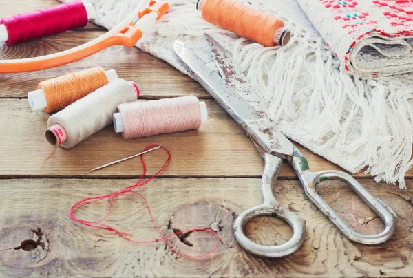 Scissors, bobbins with thread and needles, striped fabric. Old sewing tools on the old wooden background. Vintage Background